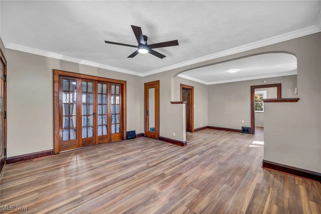 Spare room with crown molding, arched walkways, wood finished floors, ceiling fan, and a textured ceiling