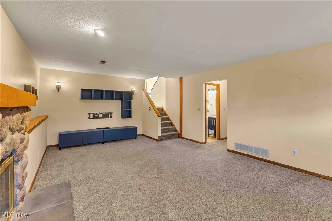 Cozy and spacious family room with a stone faced, wood burning fireplace, neutral color carpeting and overhead lighting.