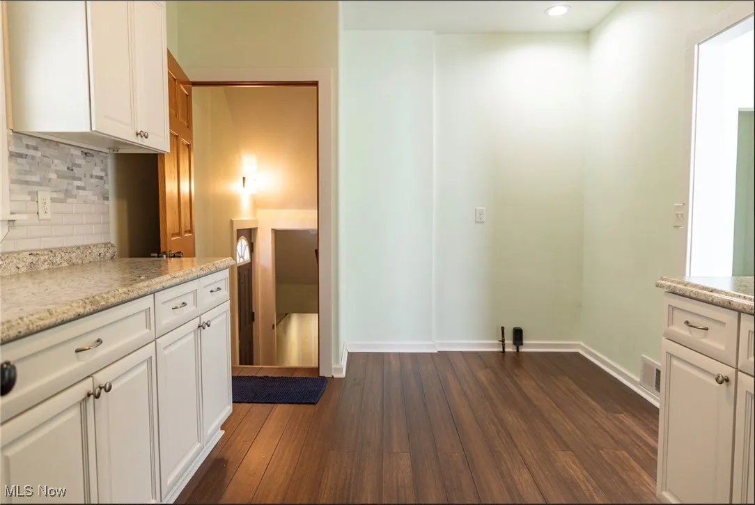 Kitchen with modern backsplash and countertops, bamboo floors, white cabinetry, and recessed lighting; with view of entry to side door and basement, or dining room area to the right