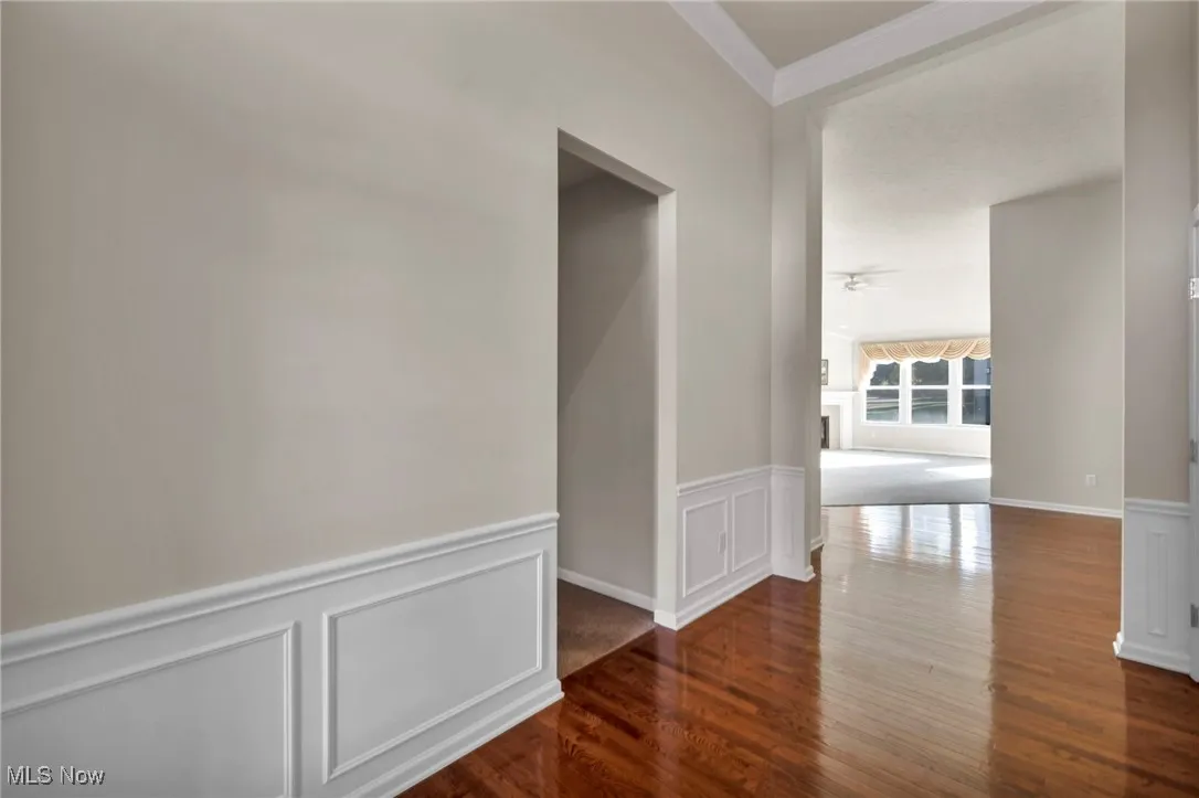 Corridor with wainscoting, a decorative wall, dark wood-style floors, and ornamental molding