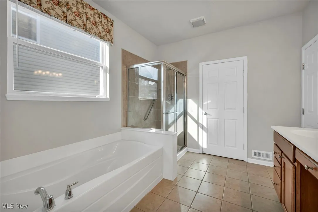 Full bath featuring a bath, vanity, light tile patterned floors, and a stall shower