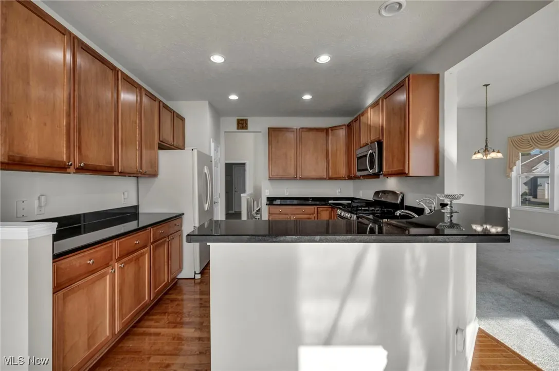 Kitchen with brown cabinets, light wood-style floors, a peninsula, stainless steel appliances, and hanging light fixtures