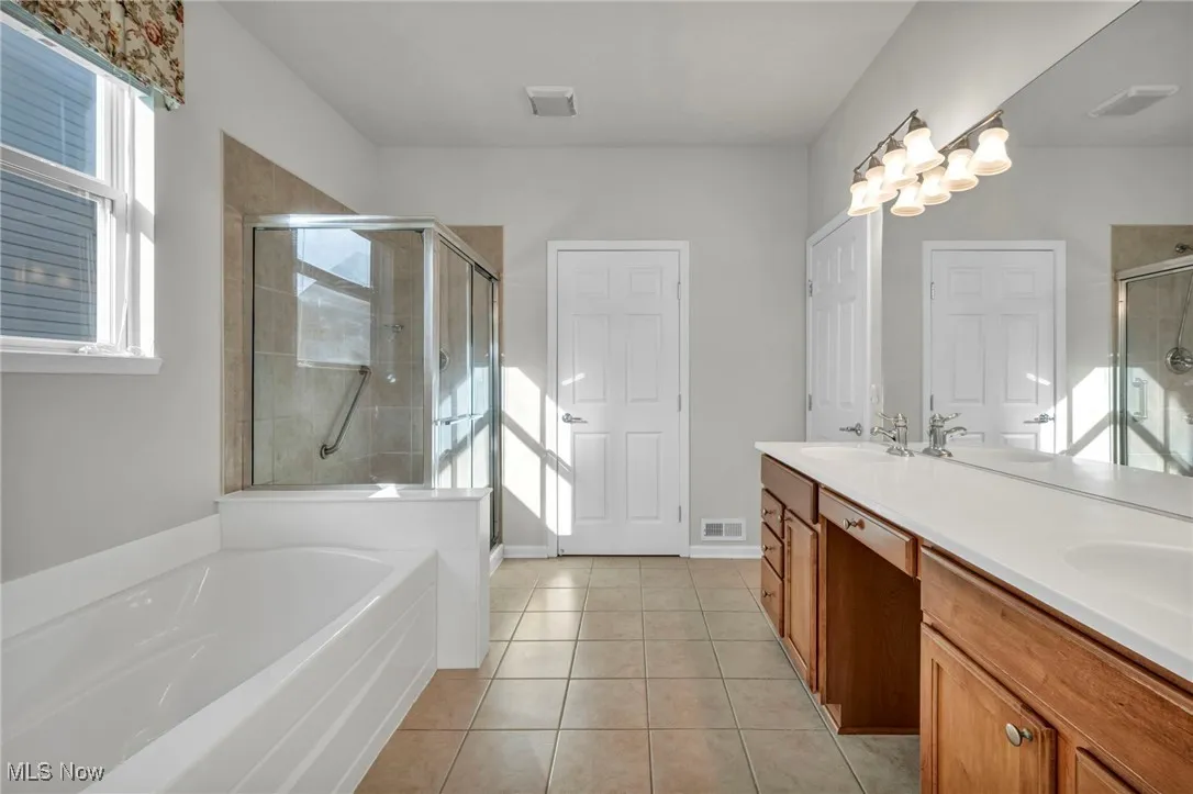 Full bath with light tile patterned flooring, a bath, a shower stall, and double vanity