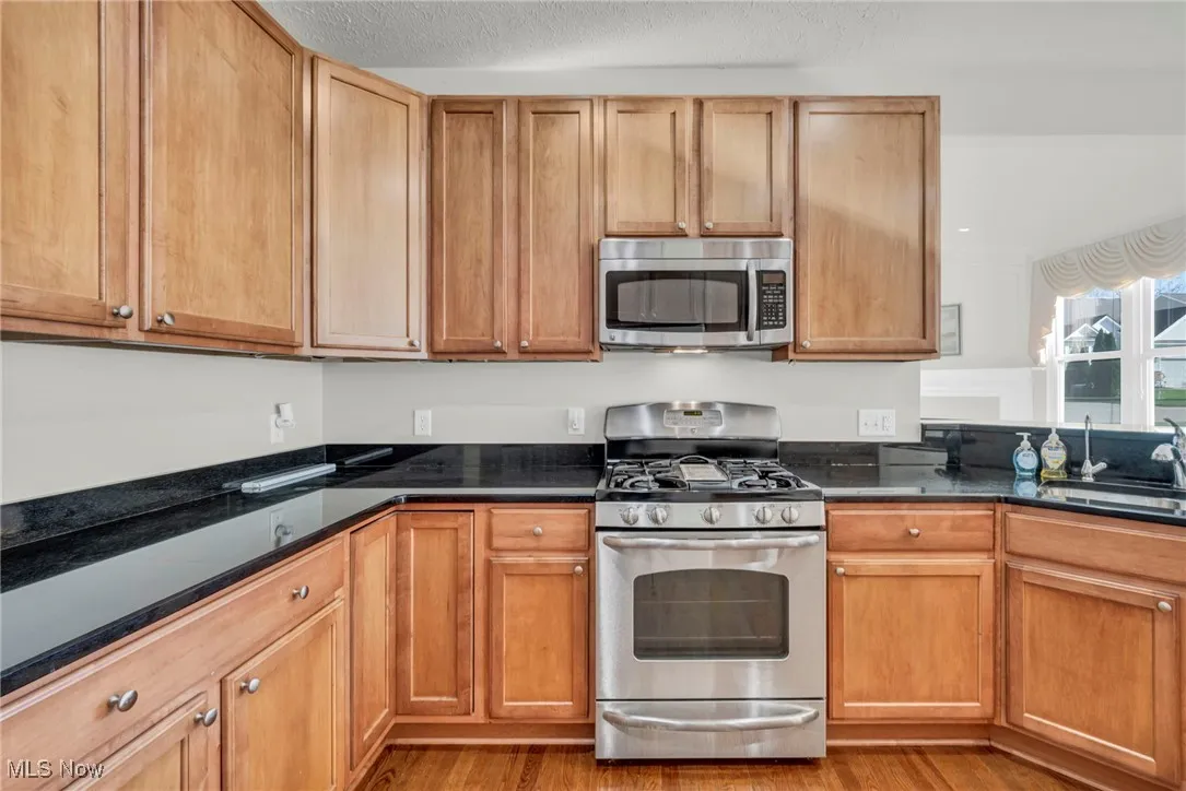 Kitchen with stainless steel appliances, dark stone countertops, light wood-style floors, a textured ceiling, and brown cabinets