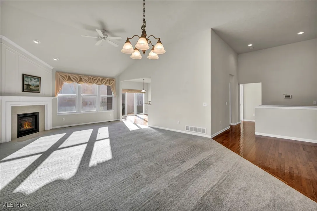Unfurnished living room with a chandelier, recessed lighting, a glass covered fireplace, ceiling fan, and dark colored carpet