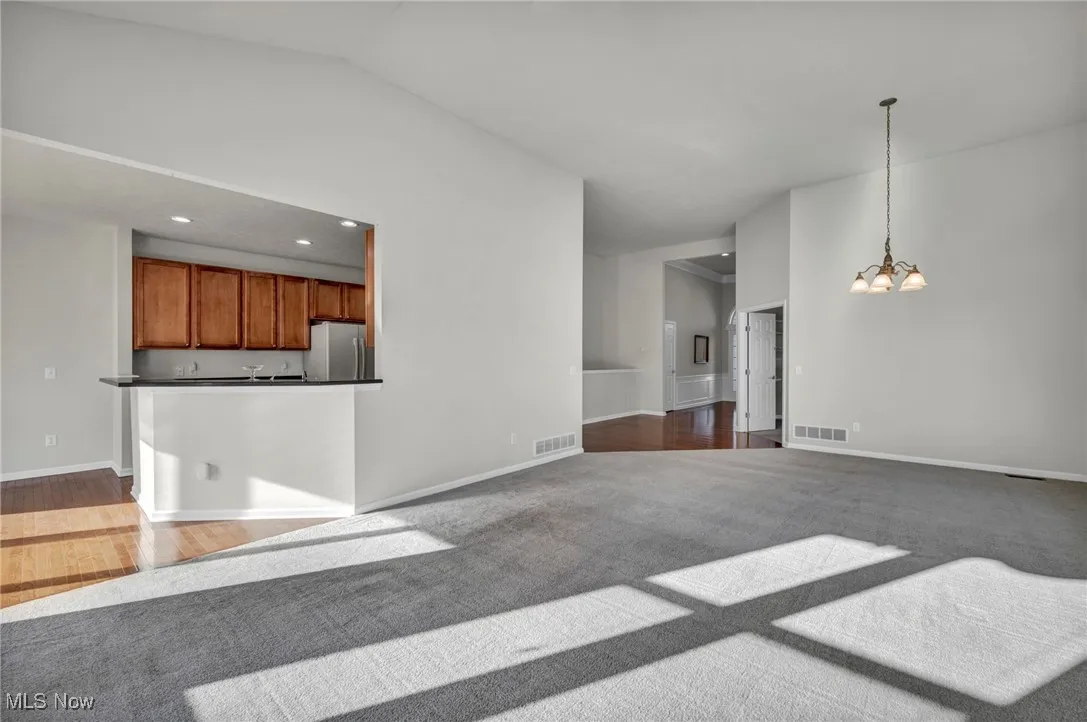 Unfurnished living room featuring a chandelier, wood finished floors, recessed lighting, carpet flooring, and lofted ceiling
