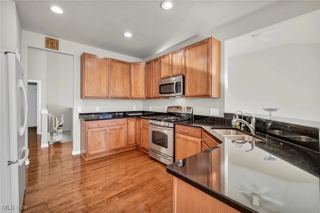 Kitchen with appliances with stainless steel finishes, dark stone countertops, light wood-style floors, recessed lighting, and brown cabinetry