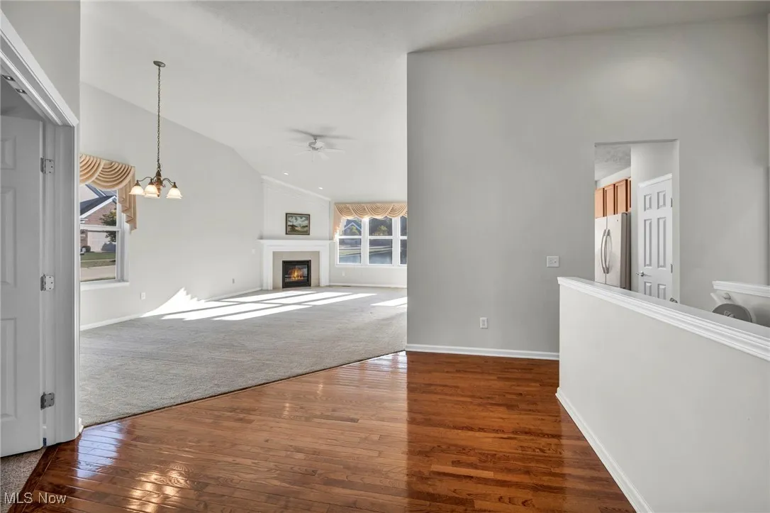Unfurnished living room featuring dark wood-style flooring, a chandelier, vaulted ceiling, a fireplace with flush hearth, and dark carpet