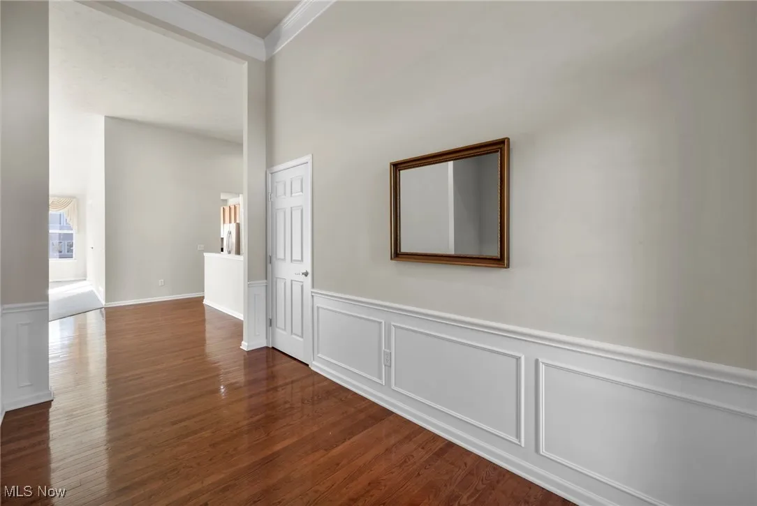 Corridor with a decorative wall, crown molding, dark wood-style flooring, and wainscoting