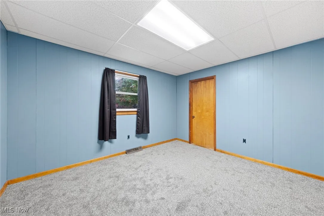 Unfurnished room with wooden walls, a drop ceiling, and carpet floors