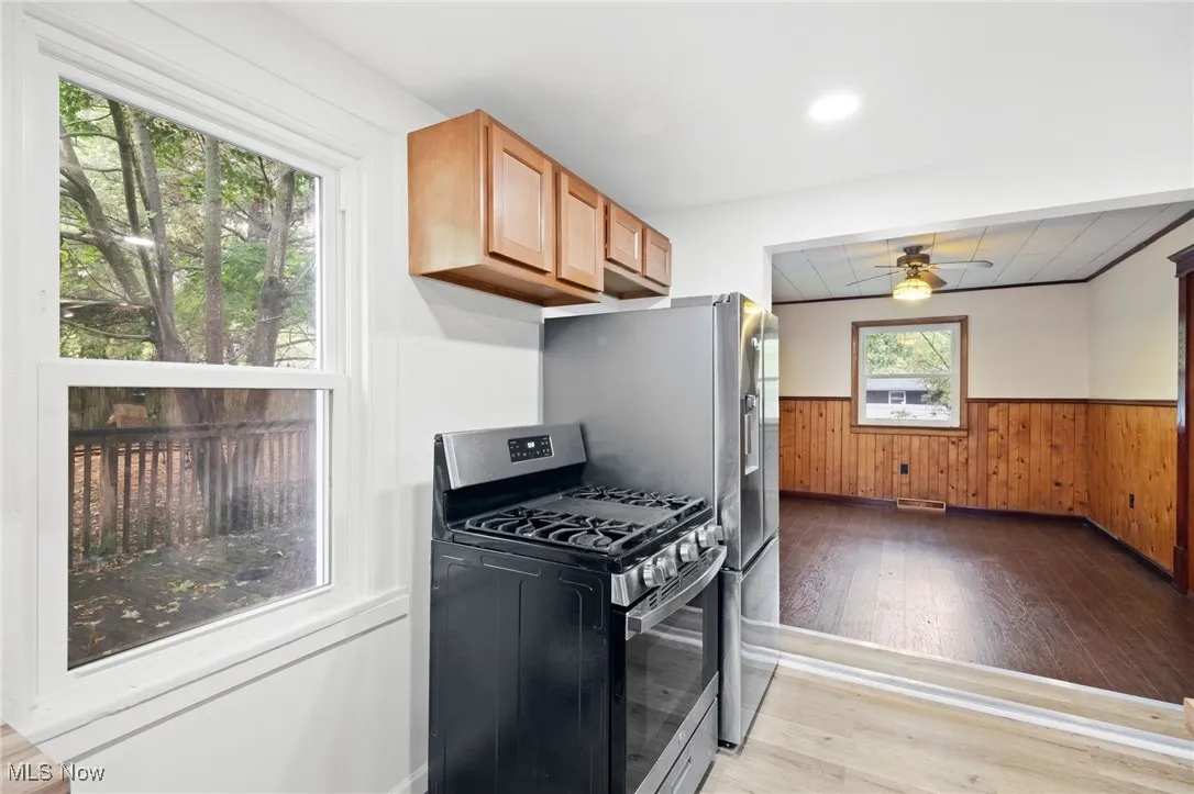Kitchen featuring light wood-style flooring, gas stove, a wainscoted wall, wooden walls, and ceiling fan