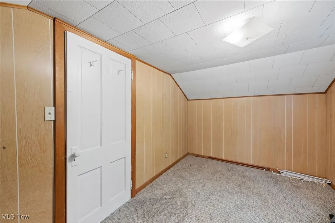 Bonus room with lofted ceiling, carpet, and wood walls