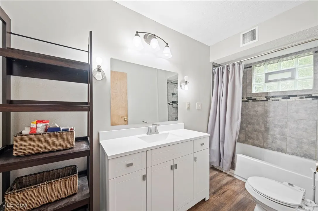 Bathroom with shower / bathtub combination with curtain, vanity, and dark wood finished floors