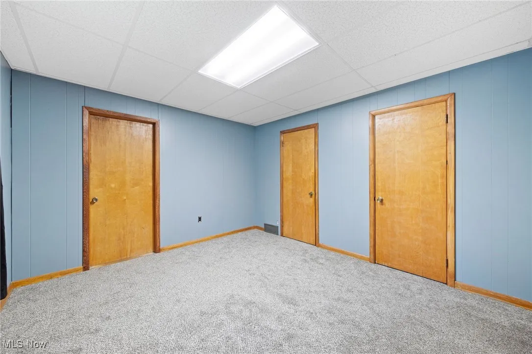 Unfurnished bedroom featuring a drop ceiling, wood walls, carpet, and a closet