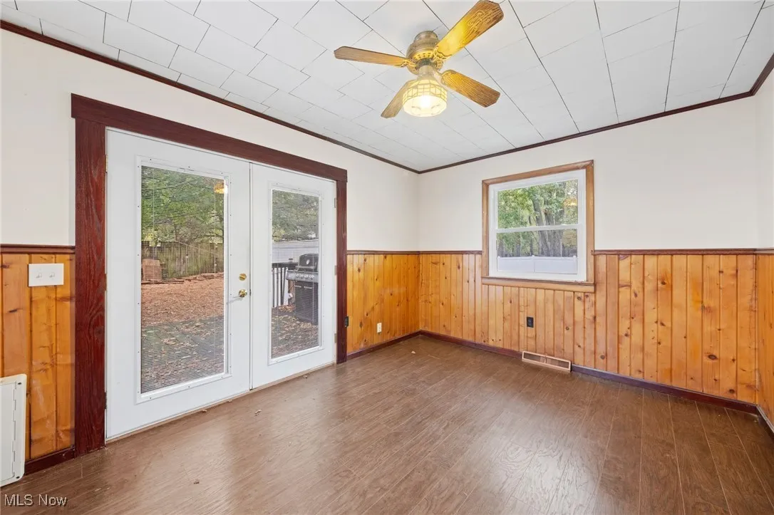 Empty room featuring wood walls, wainscoting, ornamental molding, dark wood-style flooring, and ceiling fan