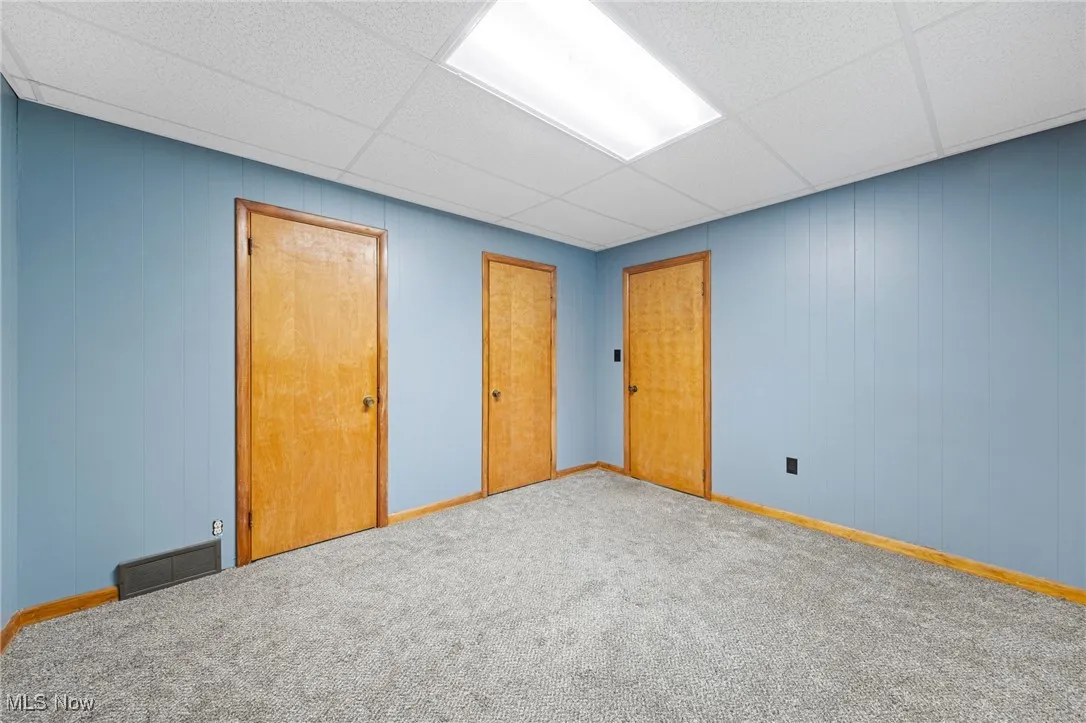 Unfurnished bedroom featuring wood walls, a paneled ceiling, a closet, and carpet flooring