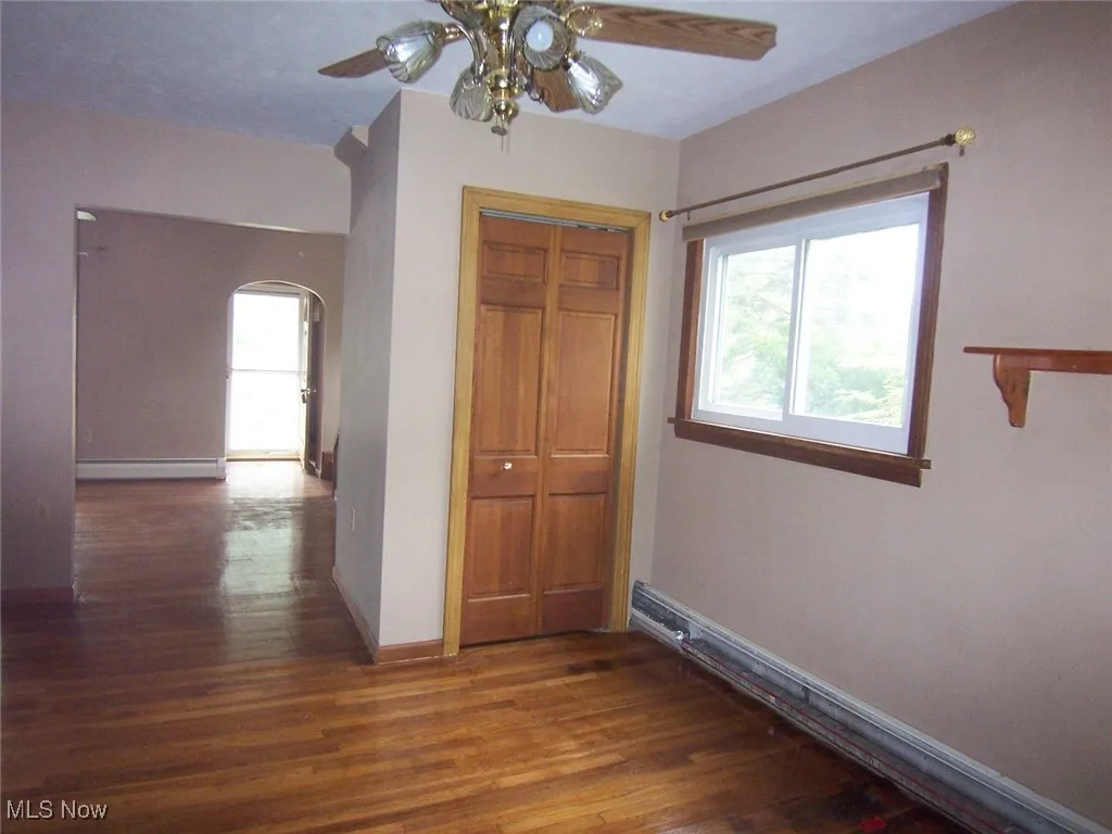 Unfurnished Dining Area open to Living Room featuring dark wood-type flooring, arched walkways, a closet, and a ceiling fan