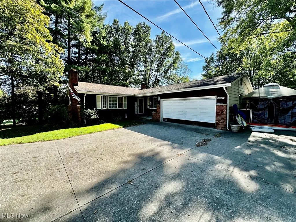 Ranch-style home with a chimney, driveway, a garage, brick siding, and a front lawn