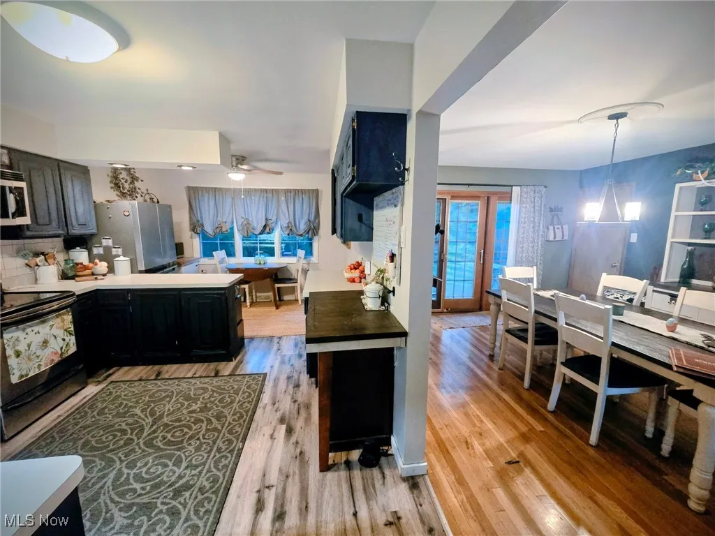 Kitchen with dark cabinetry, light countertops, black electric range oven, stainless steel microwave, and light wood-style floors
