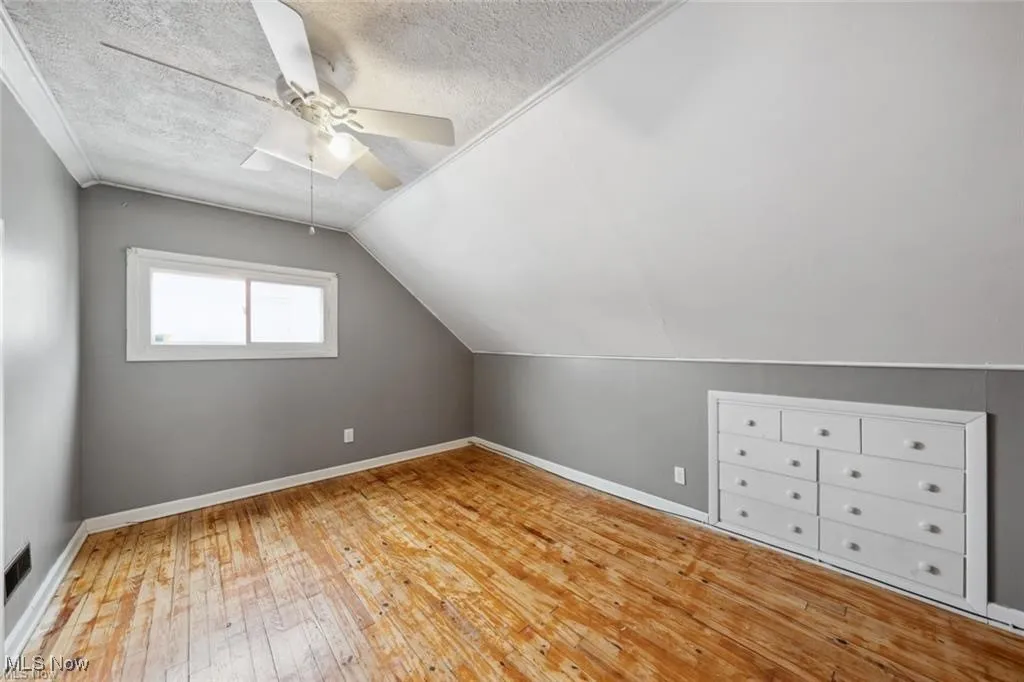 Bonus room featuring light wood finished floors, lofted ceiling, ceiling fan, and a textured ceiling