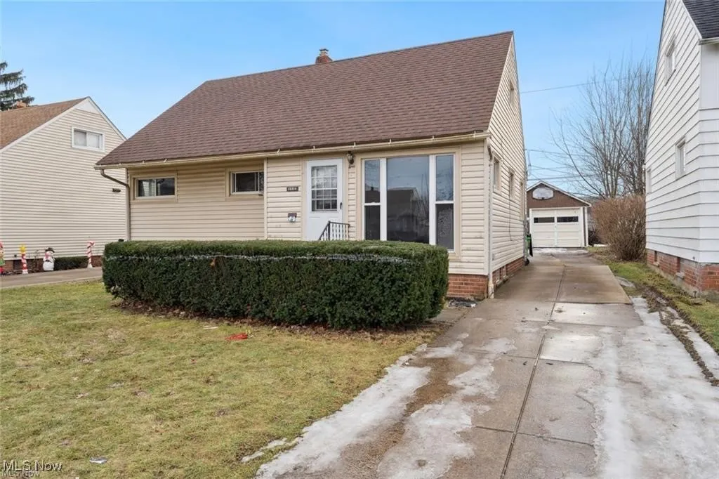 Cape cod home with a front yard, roof with shingles, an outbuilding, and a detached garage