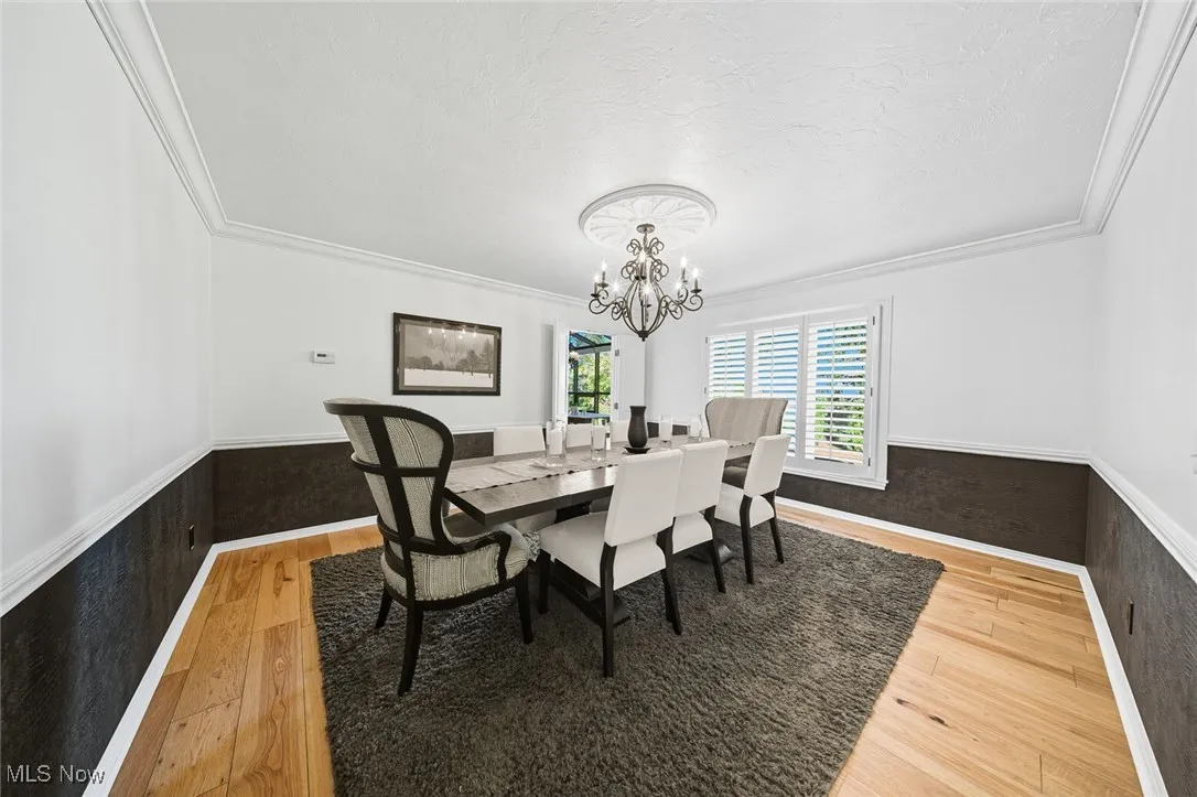 Dining space featuring a wainscoted wall, crown molding, light wood-style floors, a chandelier, and a textured ceiling