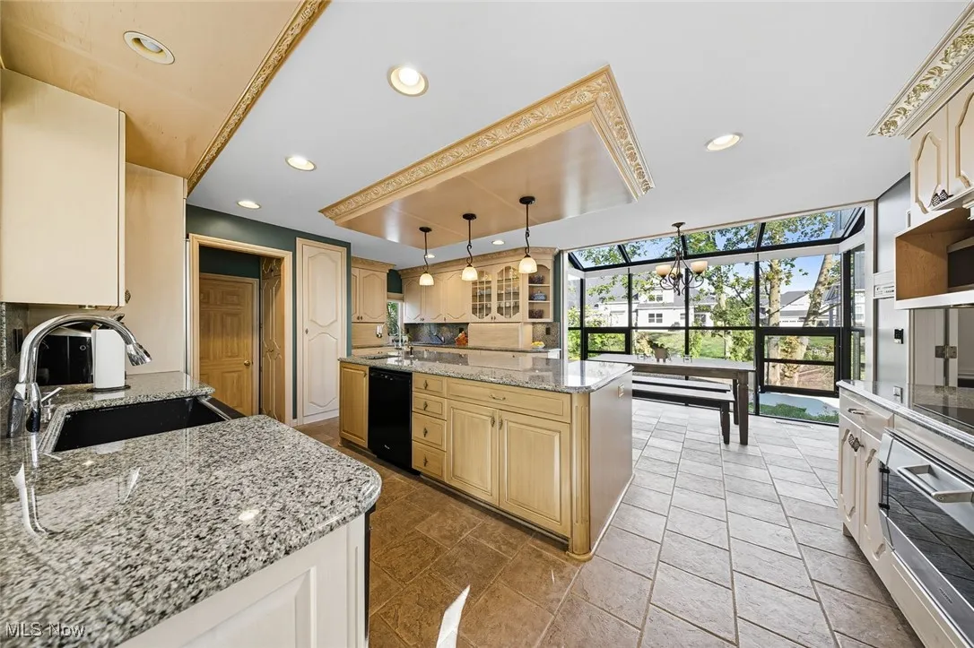 Kitchen with light stone counters, glass insert cabinets, a raised ceiling, recessed lighting, and black dishwasher