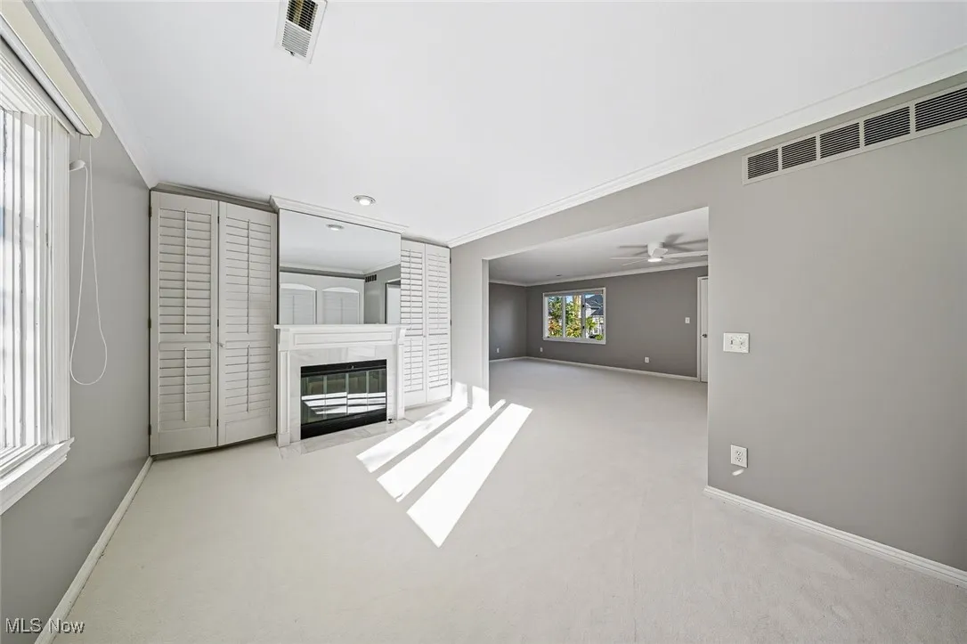 Unfurnished living room with light colored carpet, crown molding, a premium fireplace, and a ceiling fan