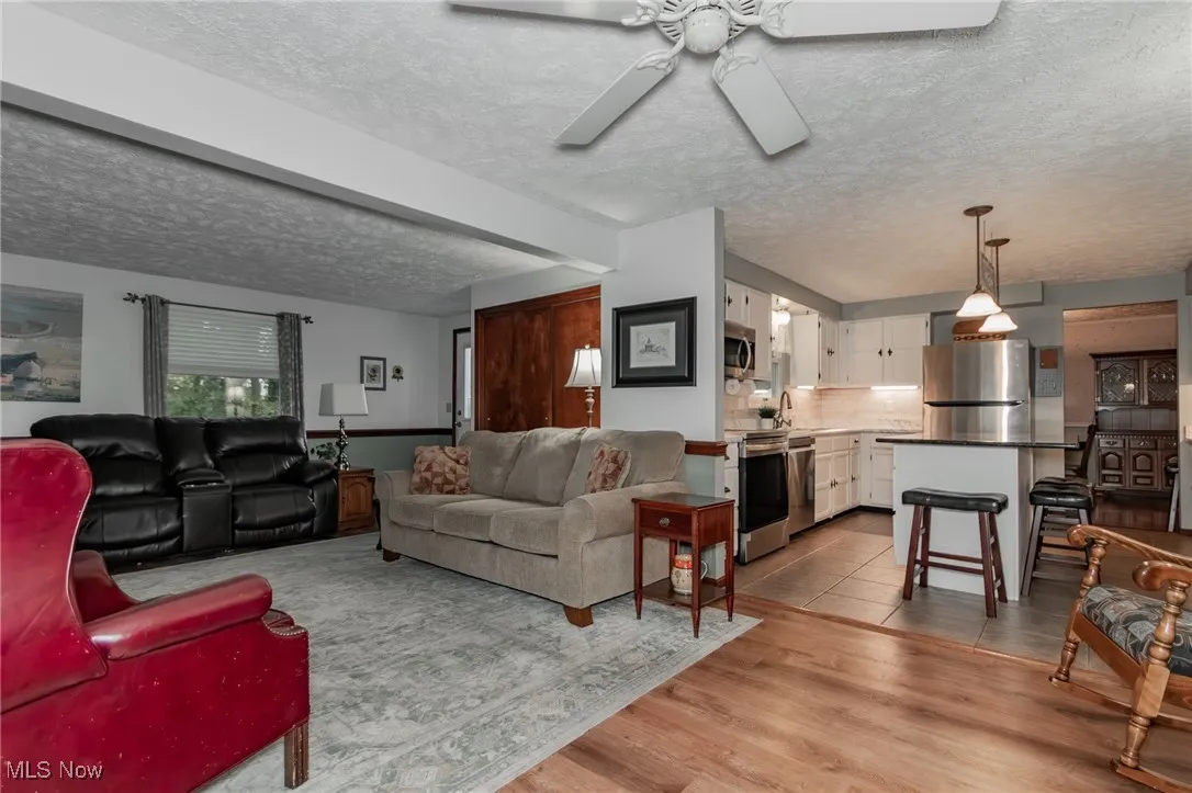 Living room with a textured ceiling, light wood-style floors, and a ceiling fan