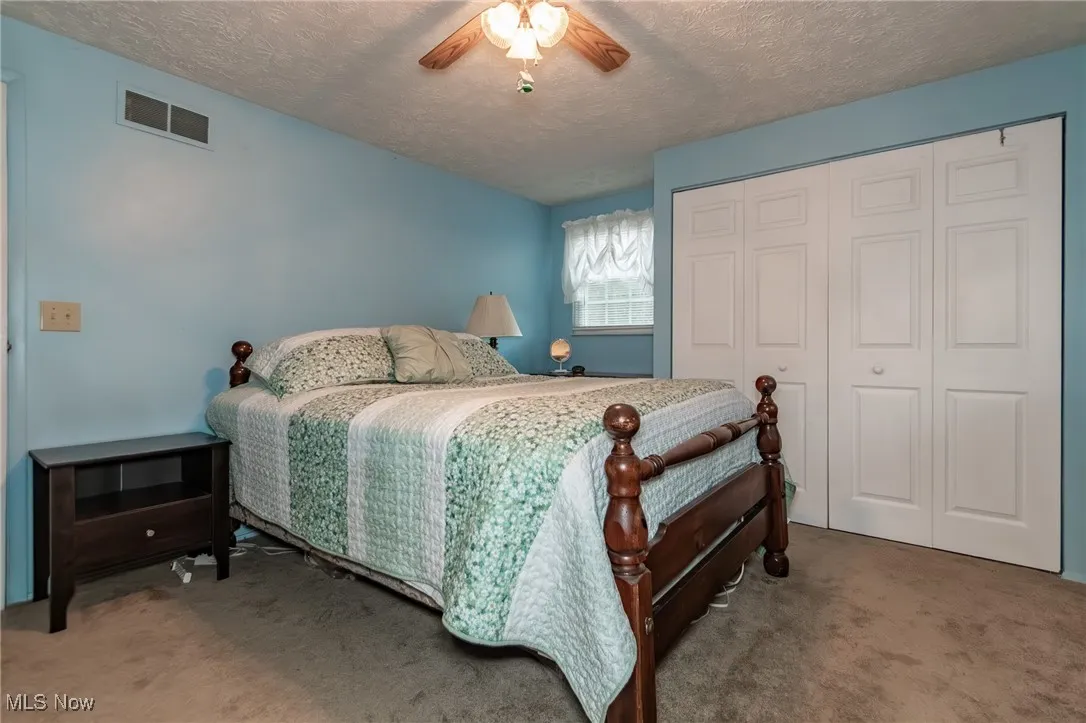 Bedroom with carpet, a closet, a textured ceiling, and a ceiling fan
