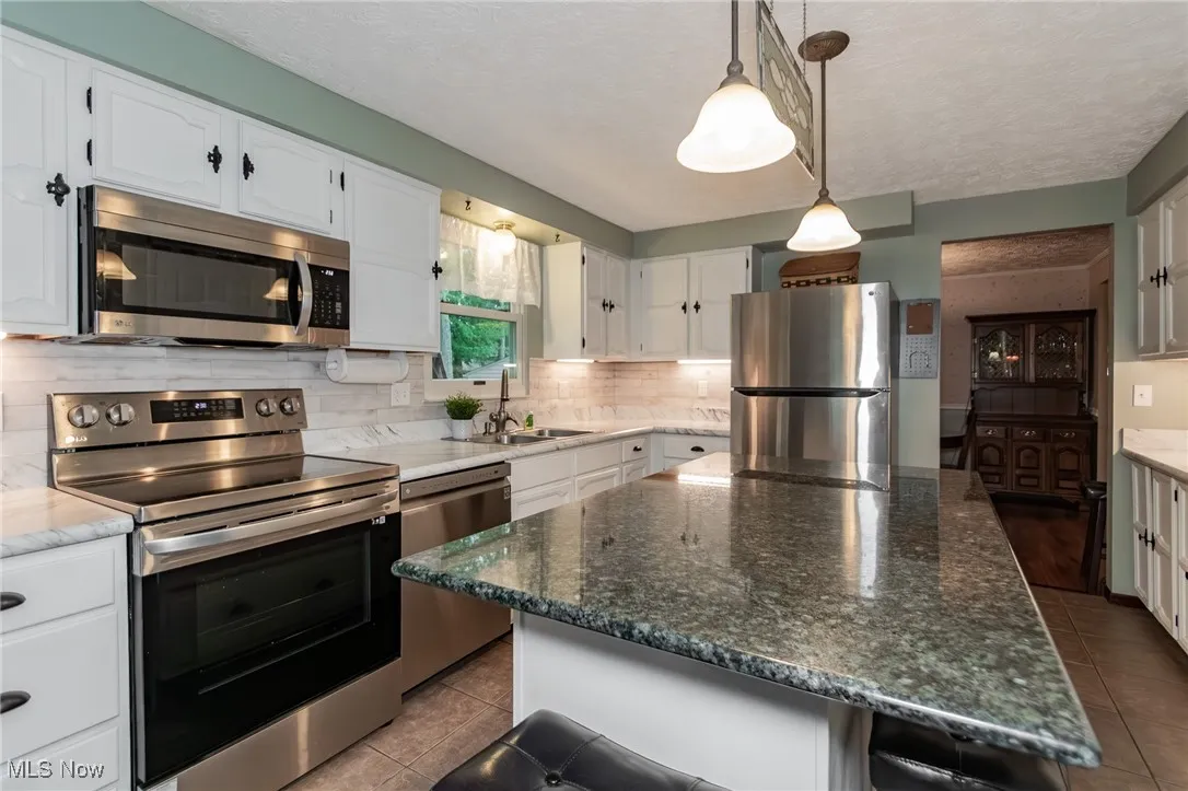Kitchen featuring stainless steel appliances, dark stone counters, pendant lighting, a center island, and white cabinetry