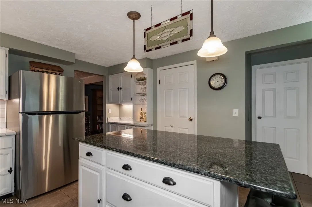 Kitchen featuring a textured ceiling, dark stone countertops, freestanding refrigerator, white cabinetry, and dark tile patterned floors