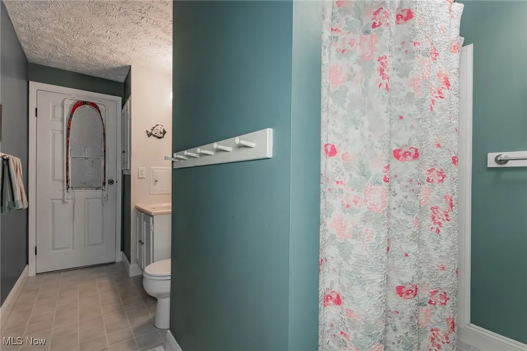 Bathroom with vanity, light tile patterned floors, a textured ceiling, and a shower with shower curtain