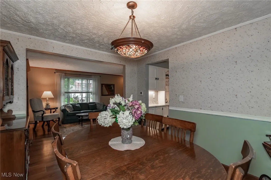 Dining room with wallpapered walls, crown molding, wood finished floors, and a textured ceiling