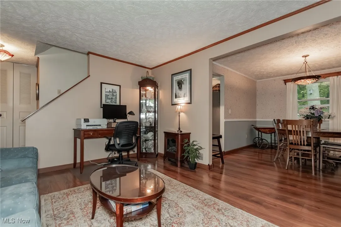 Living room with a textured ceiling, wood finished floors, ornamental molding, an office area, and wallpapered walls