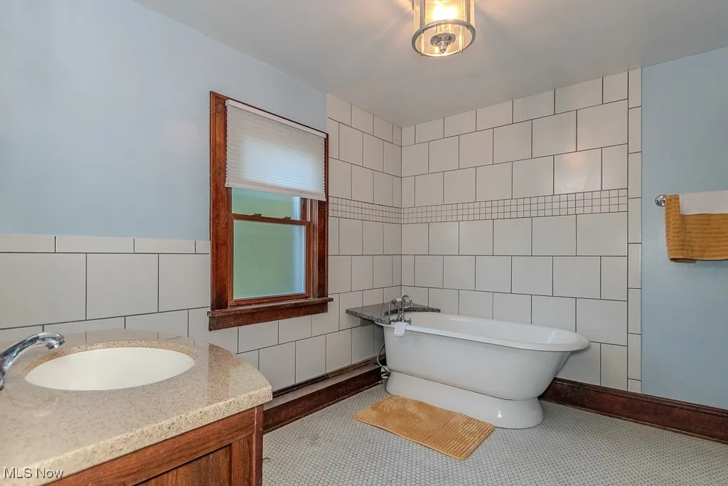 Full bathroom with a soaking tub, vanity, tile walls, and tile patterned flooring
