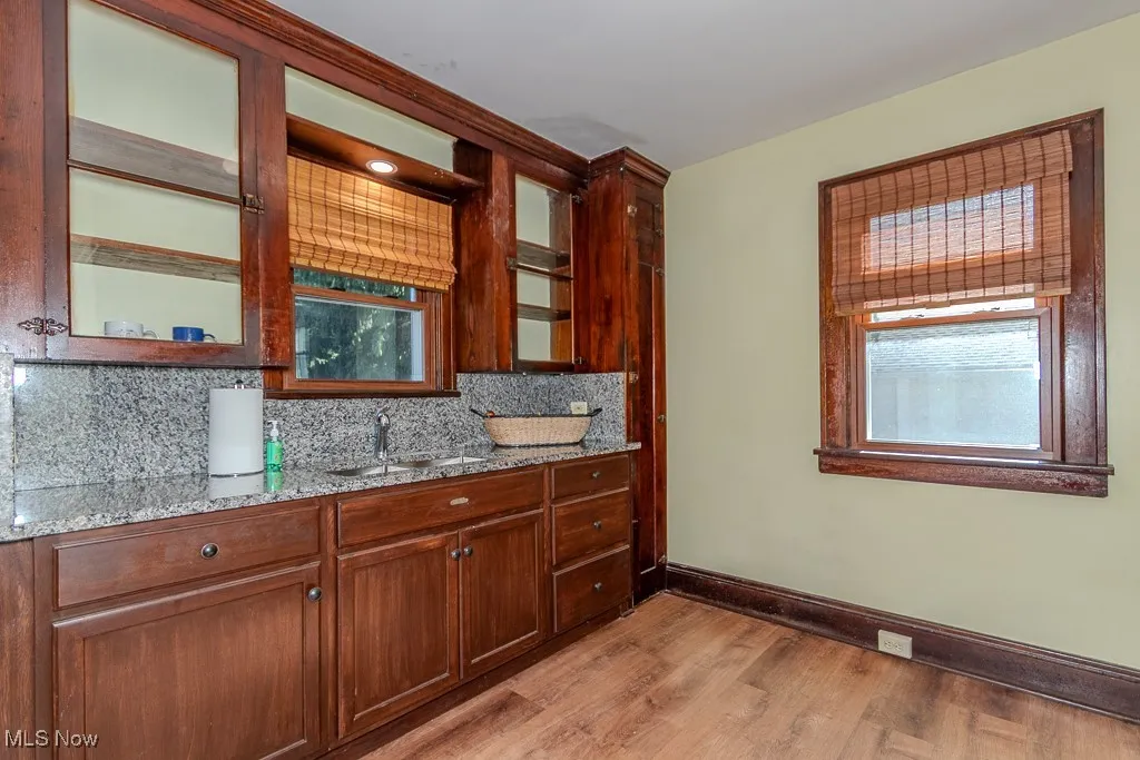 Kitchen featuring light wood-type flooring, light stone counters, backsplash, and glass insert cabinets