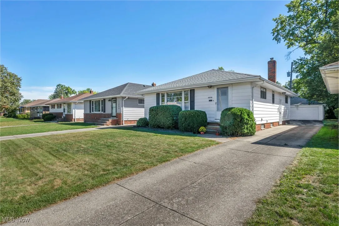 Single story home featuring a front lawn, an outbuilding, a chimney, and a detached garage