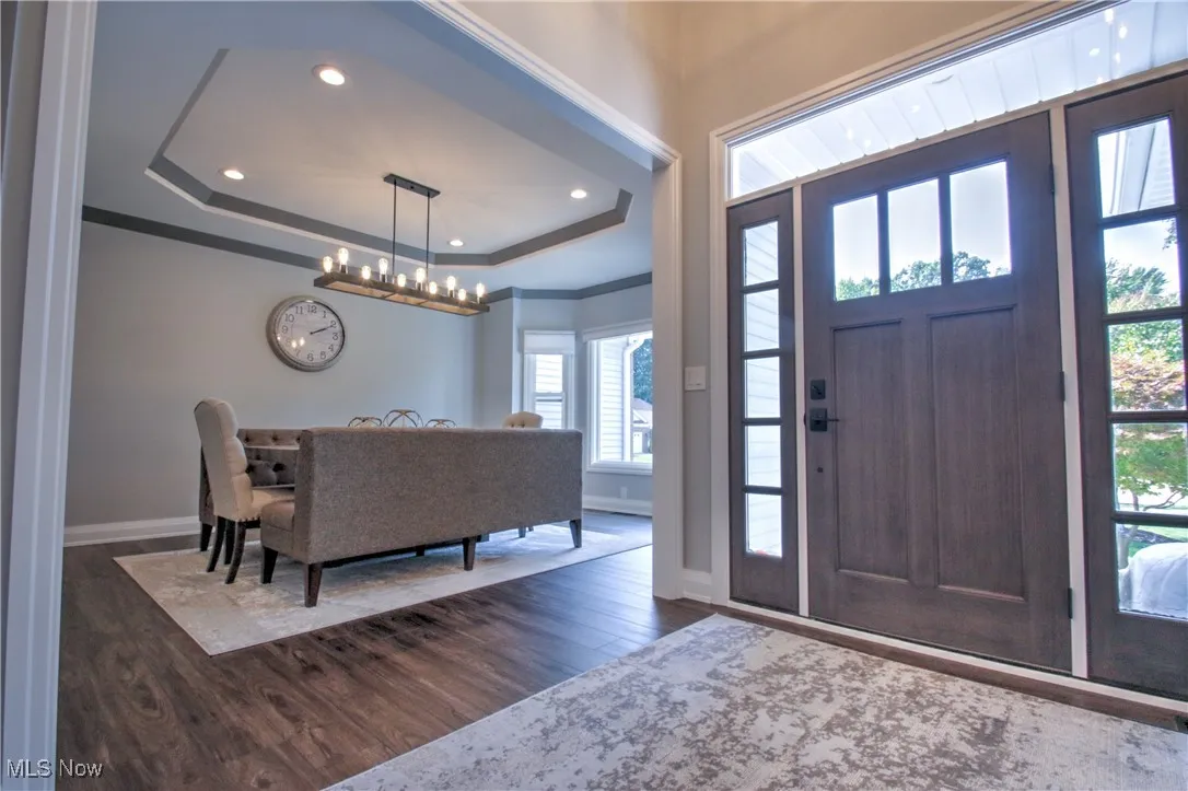 Entrance foyer featuring a tray ceiling, dark wood-type flooring, recessed lighting, a chandelier, and crown molding
