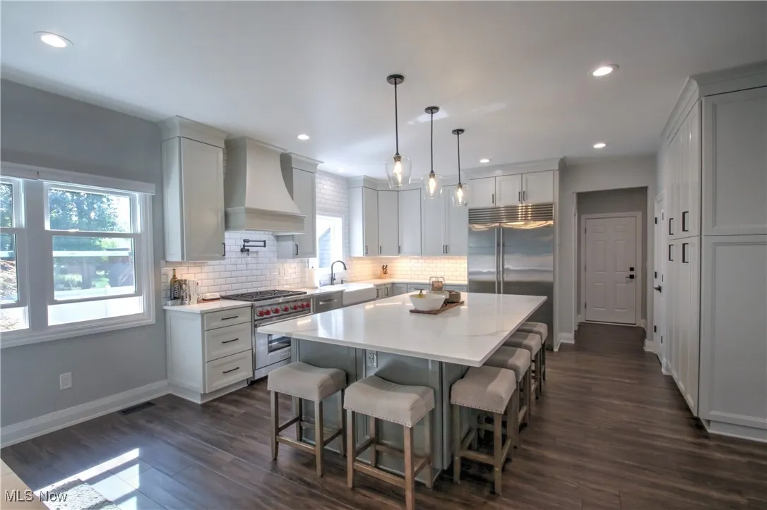 Kitchen with a kitchen bar, decorative light fixtures, custom range hood, high end appliances, and a center island