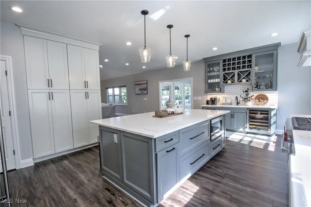 Kitchen with gray cabinetry, decorative light fixtures, dark wood-style flooring, light stone counters, and recessed lighting