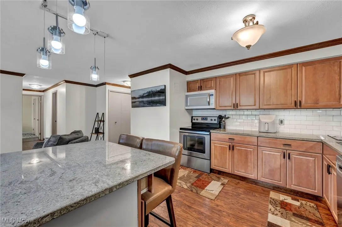 Kitchen with light stone counters, ornamental molding, stainless steel range with electric cooktop, tasteful backsplash, and a kitchen breakfast bar