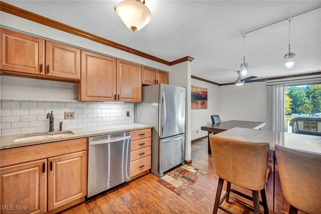 Kitchen featuring light stone countertops, appliances with stainless steel finishes, crown molding, backsplash, and light wood-style floors