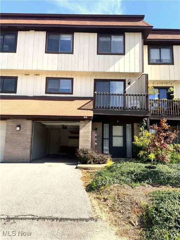 View of front of home featuring a balcony, brick siding, driveway, and a garage