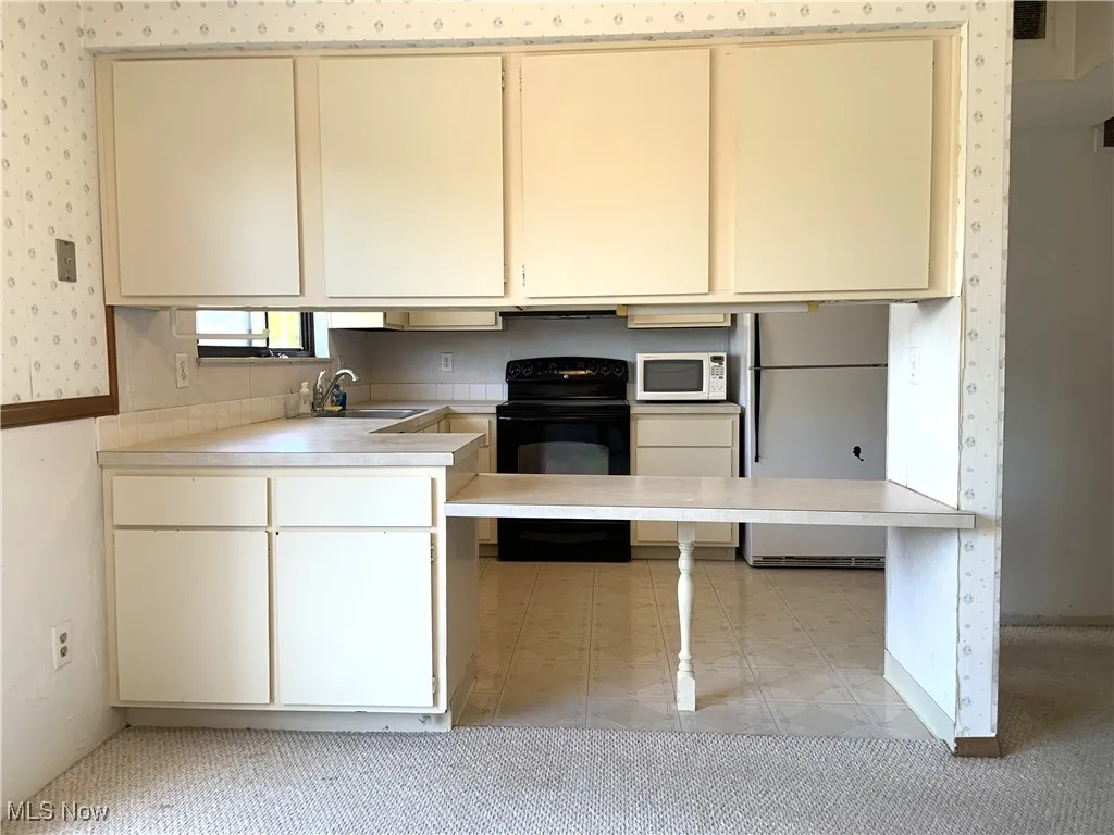 Kitchen featuring white appliances, cream cabinets, light countertops, and wallpapered walls