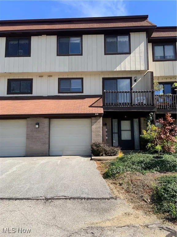 Townhouse featuring a balcony, driveway, brick siding, and an attached garage