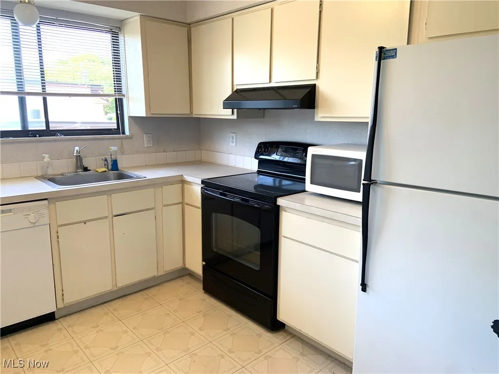 Kitchen with white appliances, light countertops, light floors, cream cabinetry, and under cabinet range hood
