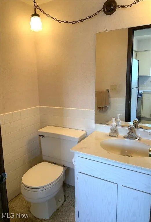 Half bathroom with tile walls, a wainscoted wall, and vanity