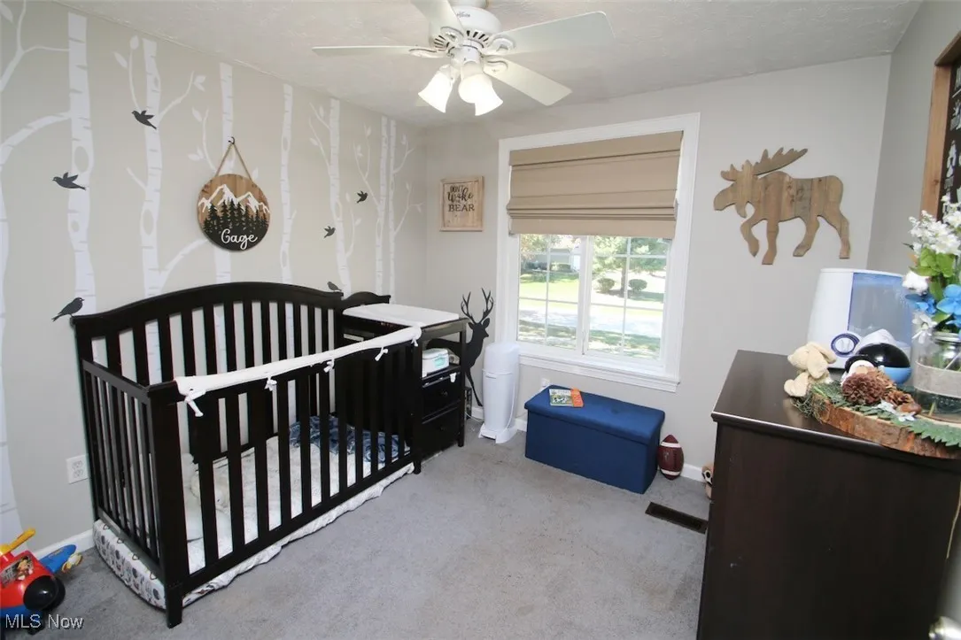 Bedroom featuring a nursery area, light colored carpet, a ceiling fan, and a textured ceiling