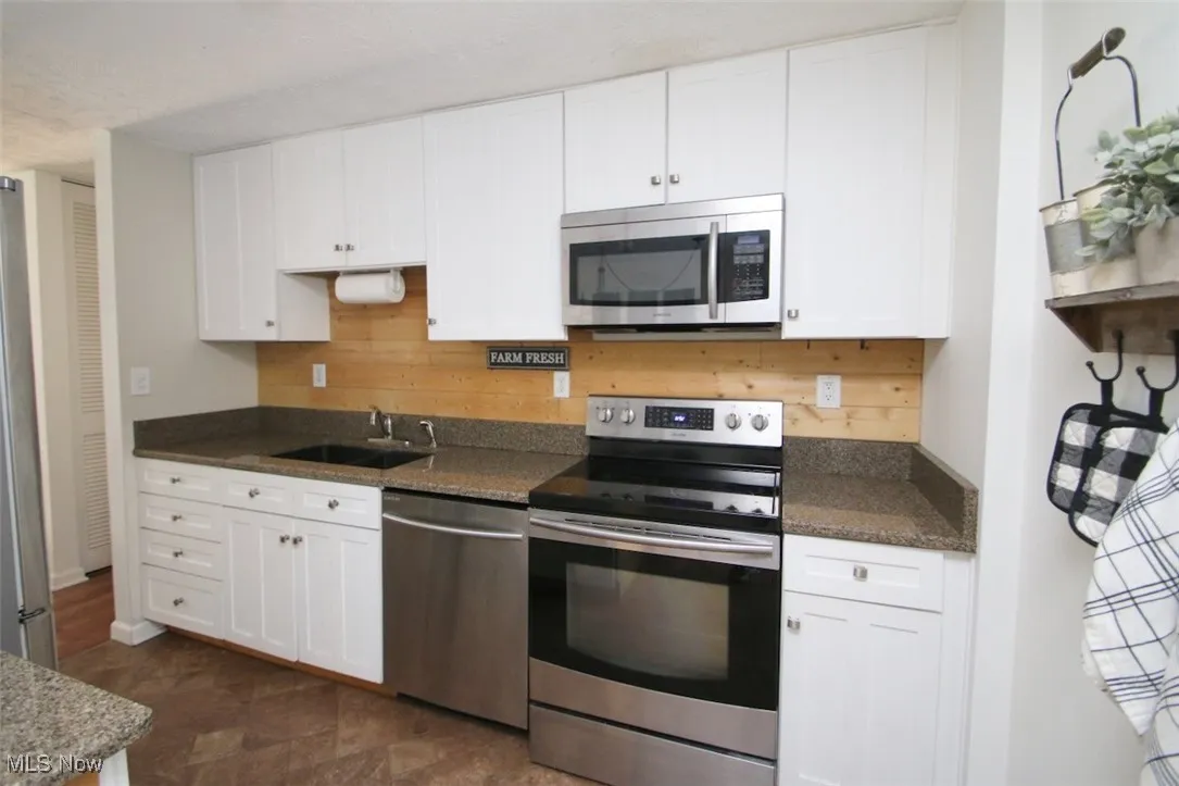 Kitchen with stainless steel appliances, white cabinets, decorative backsplash, and dark stone countertops